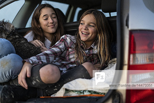 Zwei Schwestern im Kofferraum eines geparkten Autos beim Sonnenuntergang