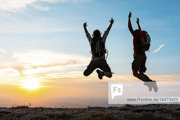 Italien  Monte Nerone  zwei glückliche und erfolgreiche Wanderer  die bei Sonnenuntergang auf den Gipfel eines Berges springen