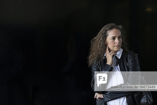 Portrait of pensive mature woman wearing black leather jacket in front of black background