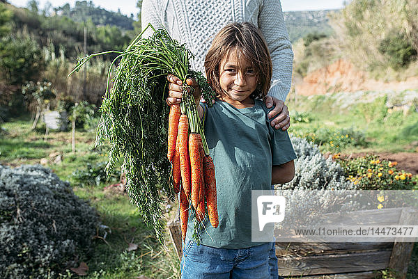 Vater steht hinter dem Sohn und hält einen Haufen Karotten