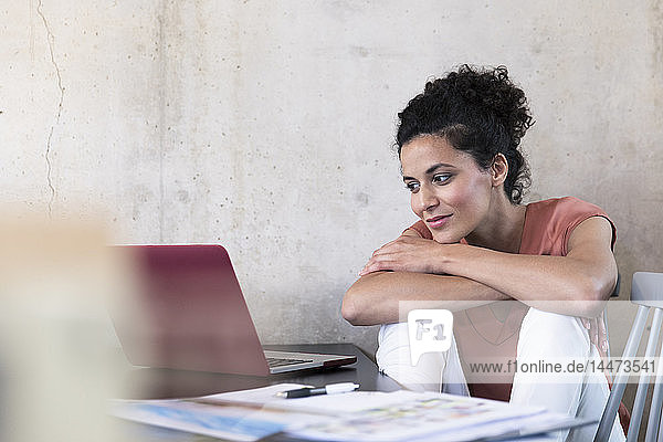 Lächelnde Geschäftsfrau sitzt am Tisch mit Dokumenten und Laptop
