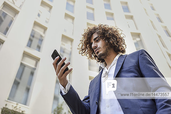 Young businessman with beard and curly hair looking at cell phone
