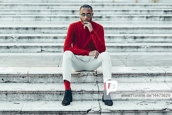 Portrait of stylish young man wearing red pullover and socks sitting on stairs