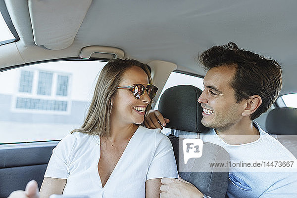 Happy couple in car with man on back seat and woman on front passenger seat