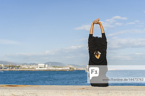 Spanien  Barcelona  Rückenansicht einer schwarz gekleideten Frau  die an einer Wand sitzt und auf das Meer schaut