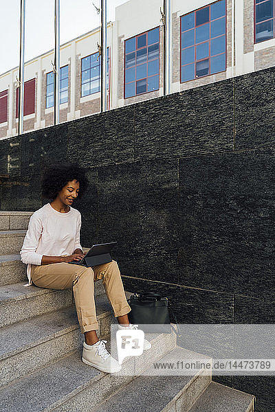Young casual businesswoman using tablet  sitting on steps
