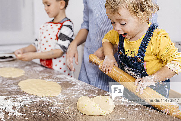 Excited toddler girl rolling out dough with wooden rolling pin