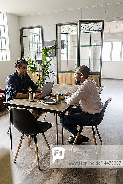 Two young businessmen talking at conference table in loft office