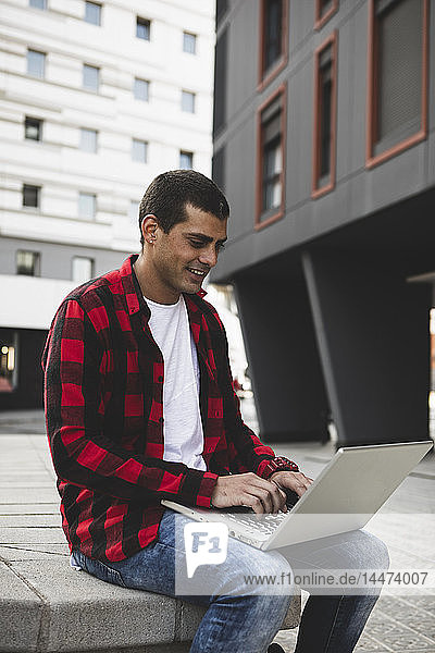 Junger Mann sitzt mit Laptop draußen in der Stadt