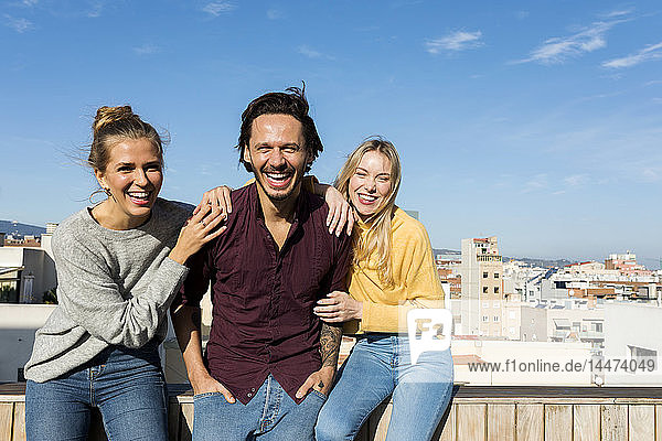 Freunde sitzen auf einer städtischen Dachterrasse  die Arme um den Kopf gelegt