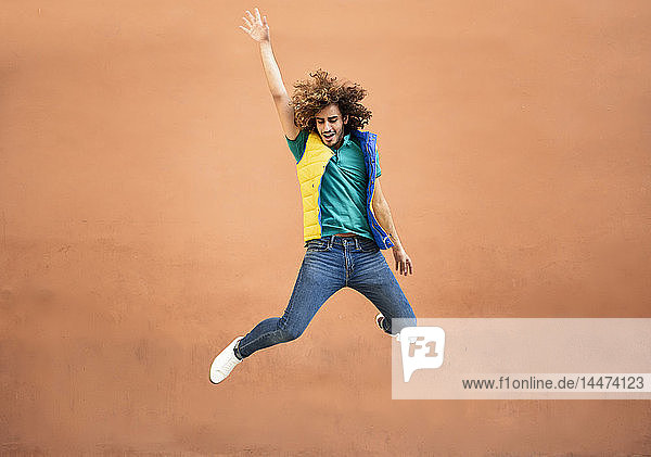 Happy young man with curly hair wearing waistcoat jumping in the air