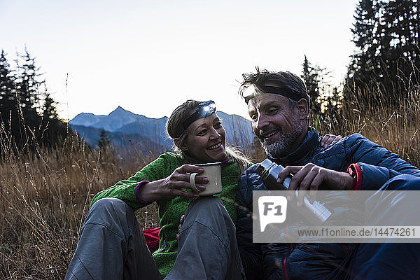Hiking couple taking a break in the evening  wearing head lamps  drinking tea