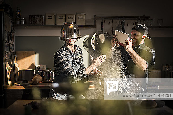 Young man filming his friend  wearing a colander as helmet in the kitchen