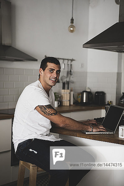 Porträt eines lächelnden jungen Mannes mit Laptop in der heimischen Küche