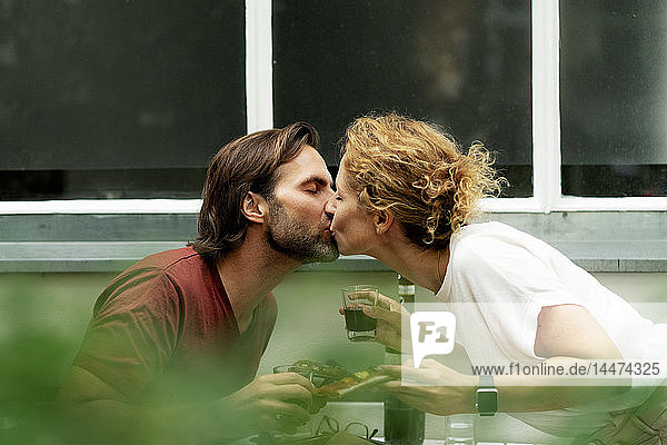 Glückliches Paar küsst sich am Tisch  isst Pizza  trinkt Wein