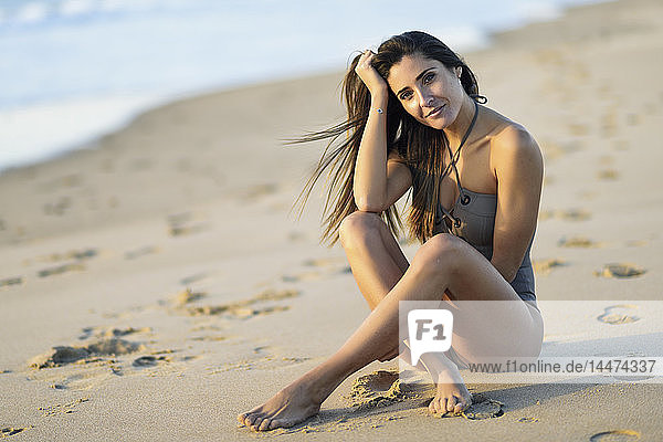 Porträt einer schönen Frau im Badeanzug am Strand sitzend