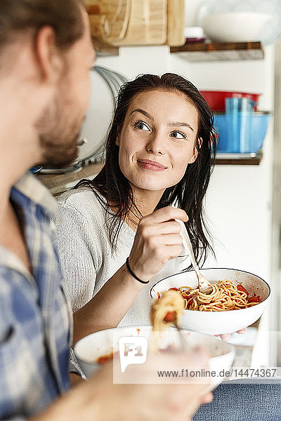 Glückliches Paar sitzt in der Küche und isst Spaghetti
