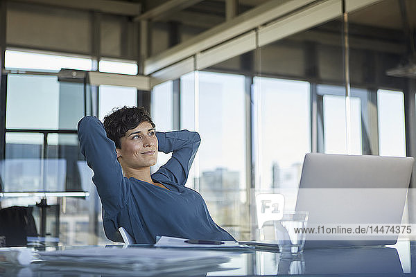 Lächelnde Geschäftsfrau sitzt mit Laptop am Schreibtisch im Büro und macht eine Pause