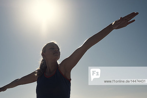 Junge Frau übt Yoga unter blauem Himmel im Gegenlicht