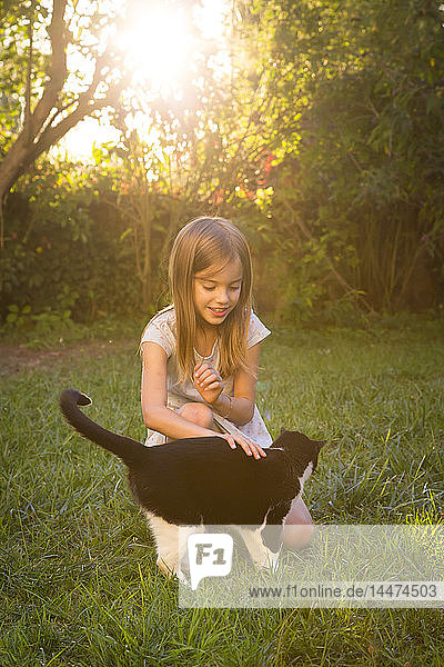 Lächelndes kleines Mädchen streichelt Katze im Garten