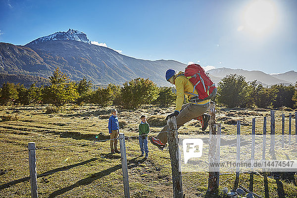 Chile  Cerro Castillo  Mutter mit zwei Söhnen auf Wanderung  die über den Zaun der Koppel springen