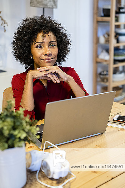 Lächelnde Frau mit Laptop am Tisch sitzend