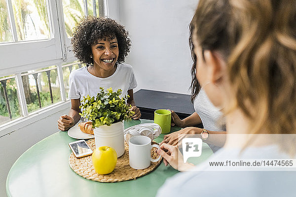 Drei glückliche Frauen sitzen zu Hause am Tisch und trinken gemeinsam Kaffee
