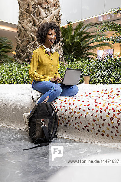 Porträt einer lächelnden Frau  die mit einem Laptop auf einer Bank sitzt