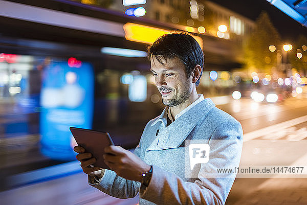 Geschäftsmann mit digitalem Tablett steht nachts an einer Bushaltestelle