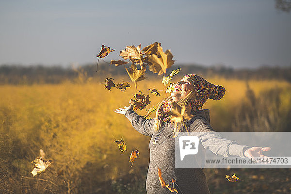 Glückliche schwangere Frau spielt mit Herbstblättern in der Natur