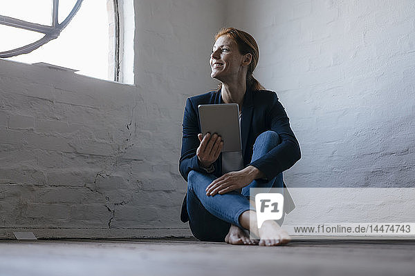 Barfüßige Geschäftsfrau sitzt im Büro mit Tablett auf dem Boden