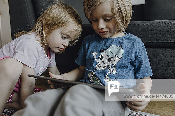 Bruder und kleine Schwester sitzen zu Hause auf dem Boden und benutzen ein digitales Tablett