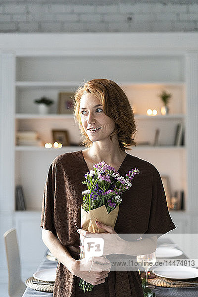 Redheaded woman holding bunch of flowers  standing in front of laid table
