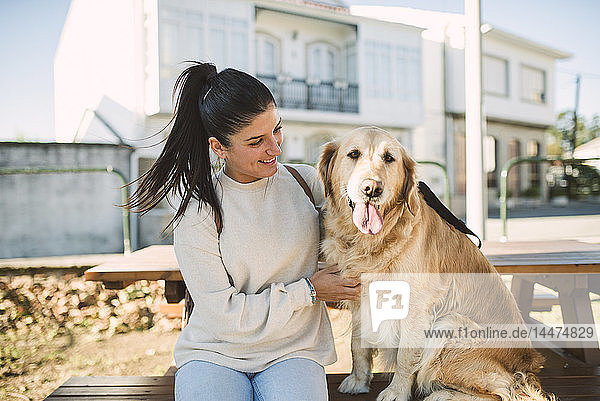 Lächelnde junge Frau mit ihrem im Freien ruhenden Golden-Retriever-Hund