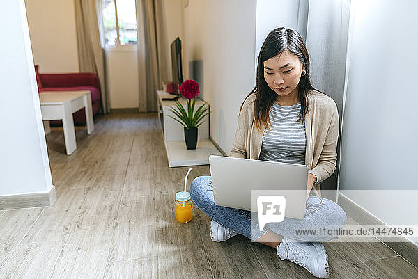 Junge Frau sitzt auf dem Boden und benutzt einen Laptop