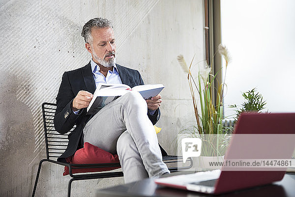 Businessman sitting at concrete wall reading book