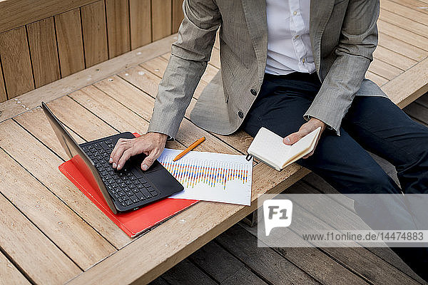 Close-up of businessman sitting on a bench using laptop and diary