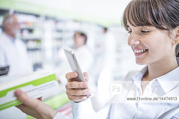 Lächelnde Frau in der Apotheke mit Smartphone und Medikamenten