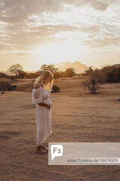 Namibia  Spitzkoppe  Frau in weißem Kleid in Wüstenlandschaft bei Sonnenuntergang