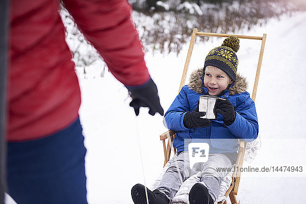 Portrait of smiling little boy drinking tea while his father pulling the sledge