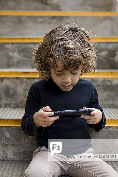 Junge sitzt auf einer Treppe und spielt mit einer tragbaren Spielkonsole