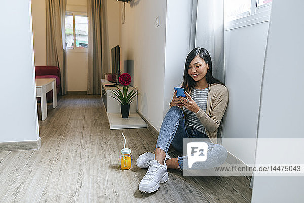 Junge Frau sitzt auf dem Boden und benutzt ein Smartphone