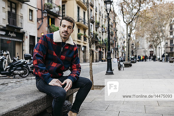 Junger Mann in legerer Kleidung sitzt auf einer Bank in der Stadt