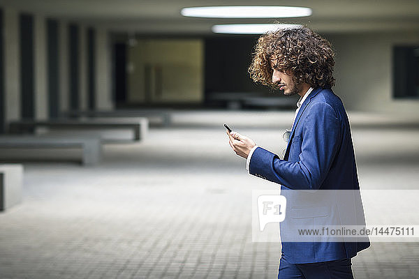 Young fashionable businessman with curly hair looking at smartphone