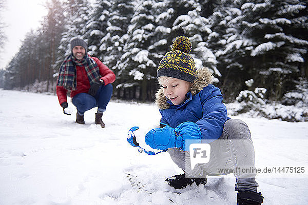 Father and little son having a snowball fight in winter forest