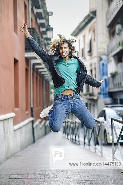 Porträt eines lächelnden jungen Mannes  der im Freien in die Luft springt
