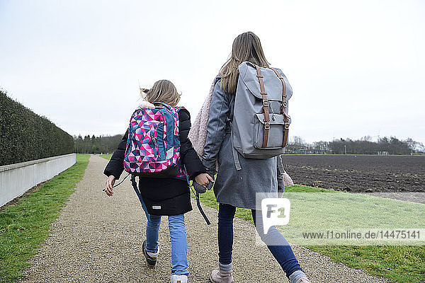 Back view of two sisters with backpacks walking hand in hand
