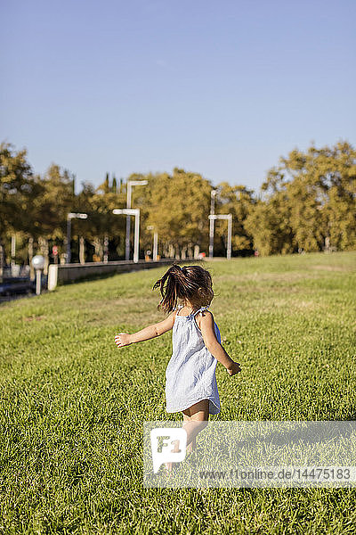 Rückansicht eines kleinen Mädchens  das auf einem Rasen in einem Park läuft