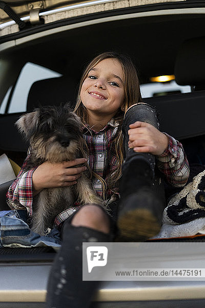 Porträt eines lächelnden Mädchens  das mit seinem Hund im offenen Stiefel sitzt