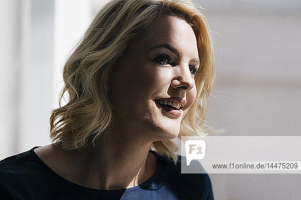Porträt einer lächelnden blonden Frau im Sonnenlicht am Fenster